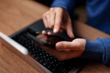 Person using smartphone while sitting at a desk in a cozy environment with a laptop nearby during daytime