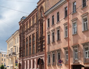 Fototapeta premium A row of orange, brown and white historic residential buildings with ornate facades and arched windows in city under a cloudy sky