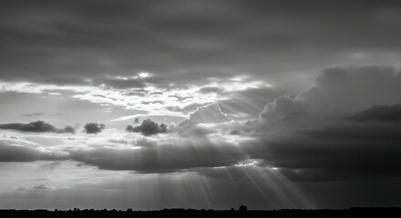 Dramatic black and white sky with heavenly sunbeams breaking through dark clouds over a silhouette horizon.