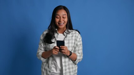 Happy smart joyful young woman of Asian ethnicity hold use pointing finger on mobile cell phone just found out great big win news isolated on blue background - Powered by Adobe