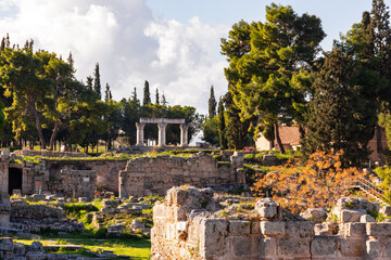 Stone ruins and Corinthian columns in the archaeological site of ancient Corinth, Greece surrounded by trees