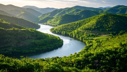 Obraz premium Serpentine river meanders through lush green hills under a partly cloudy sky