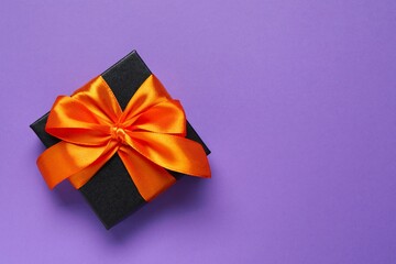 Top view photo of giftbox with orange satin ribbon bow on violet background. Top view, space for text