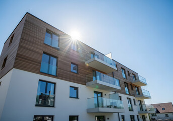 Low-angle view of a modern residential building with wood cladding and glass balconies against a sunlit blue sky