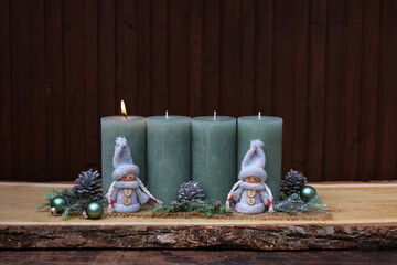 Decoration for the first Advent. An arrangement with green candles and branches, one of which is lit.