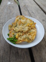 A plate of traditional Indonesian corn fritters, known as corn fritters, served with fresh green chili peppers. This savory snack features sweet corn kernels in a crispy, golden-brown batter.