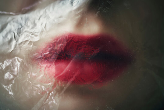 Red lips with lipstick under plastic foil symbolizing asphyxiation and beauty