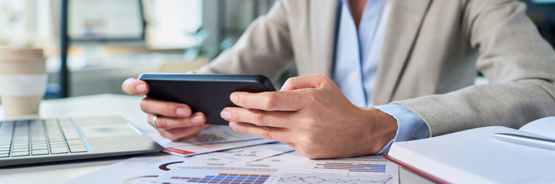 Businesswoman using smartphone at desk with paperwork in office