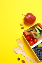 Vertical photo of lunchbox with healthy snacks and fruits on a yellow background