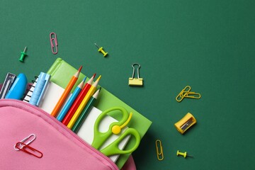 Pink backpack with school supplies on green background