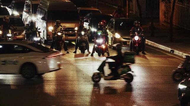 Dynamic night scene of traffic at a busy intersection in Bangkok Motorcycles and cars navigate the urban streets showcasing vibrant city life amidst illuminated vehicles