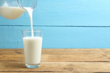Closeup of pouring fresh milk from jug into glass at wooden table  