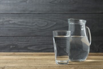 Glass of water with jug at wooden table, closeup. Drinking clear water in the morning for health. Space for text 