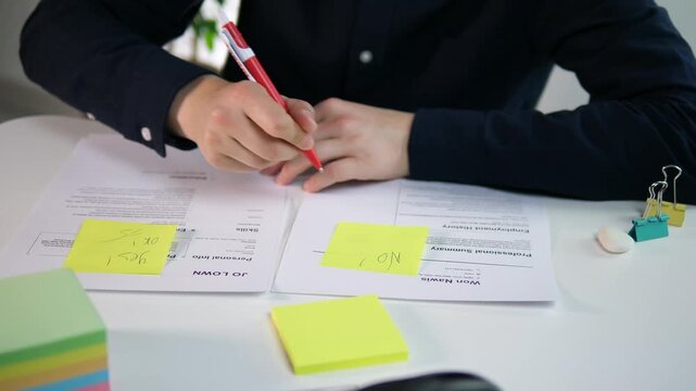 Hands of a male recruiter or manager holding candidates' resumes, marking them yes and no. Reviewing resumes, recruiting employees.