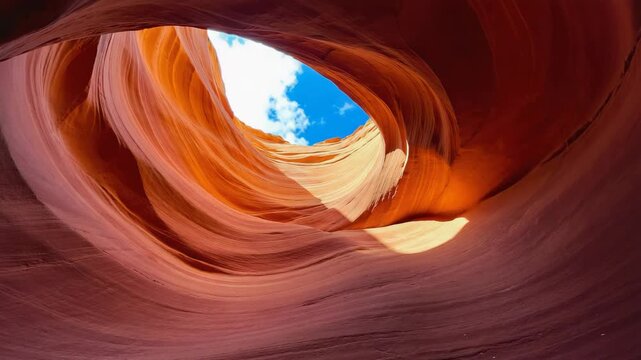 View from inside Antelope Canyon reveals swirling red sandstone walls curving toward a bright patch of open sky, highlighting the sculpted textures, natural light, dramatic desert erosion over time.
