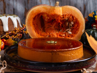 A glistening pumpkin flan, adorned with pumpkin seeds, sits on a dark plate.
