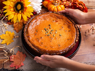 Pumpkin pie topped with pumpkin seeds, on a wooden table, surrounded by autumn leaves and sunflowers
