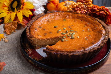 Pumpkin pie topped with pumpkin seeds, on a wooden table, surrounded by autumn leaves and sunflowers