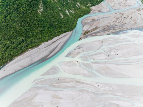 Iconic Italian river Tagliamento, Friuli, Carnia, Italy. The braided river flows through a wide gravel bed, bordered by a lush green forest on one side.