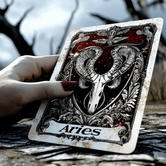 Gothic-style Aries zodiac tarot card featuring a ram skull, held by a hand in a mysterious, dark forest setting.
