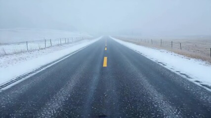 Straight two-lane highway stretches into the distance through snowy winter landscape with blowing wind and mist, creating a sense of isolation, adventure, and travel through a cold weather environment - Powered by Adobe
