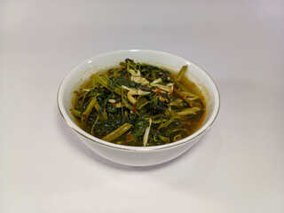 White ceramic bowl filled with a hearty serving of cooked water spinach in a savory, slightly oily sauce or broth. Related to healthy eating, Asian cuisine, vegetable dishes, home cooking, nutritious