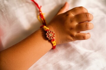 A child's wrist adorned with a red and yellow rakhi against a soft white fabric background close up view