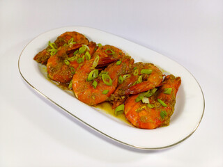 Serving of large, cooked prawns on a white oval platter with a gold rim. The prawns are bright orange-red, coated in a savory, textured sauce. Related to seafood cuisine, gourmet cooking, healthy eats