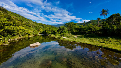 Landscape in the depths of a humid tropical forest. River valley in a hilly area covered with jungle. View of a shallow river flowing through a picturesque valley surrounded by hills and mountains.