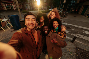 Group of happy multiracial friends taking photo of themselves in urban street during sunset