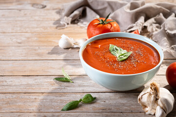Homemade Tomato Soup in bowl with Basil on wooden table. Copy space