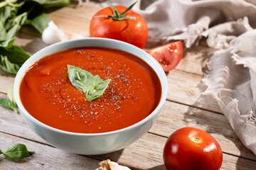 Homemade Tomato Soup in bowl with Basil on wooden table. Copy space