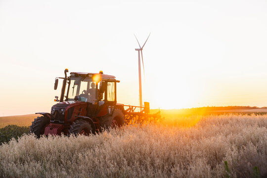 Tractor and farmer in field at sunset with wind turbine in background