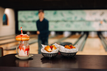 Teenager approaching two hotdogs and strawberry milkshake with donut on top at bowling alley