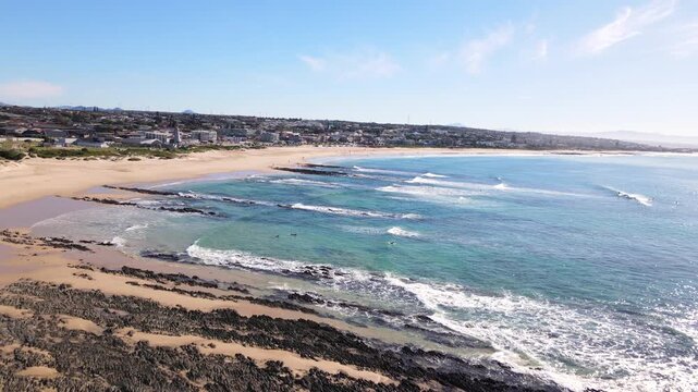 Drone pullback view of surfers paddling out from Jeffreys Bay main beach
