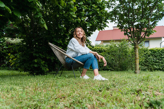 Fototapeta Smiling woman relaxing in garden chair embracing slow eco lifestyle