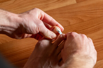 Man trims big toe nail with manicure scissors. A man trimming his big toe nail using manicure scissors