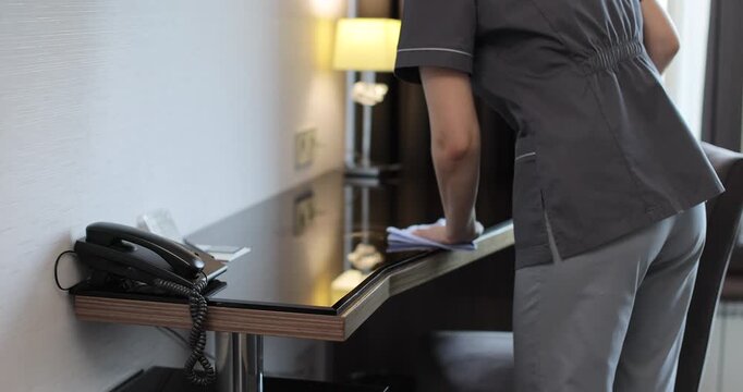 Close up of hotel housekeeper applying cleaning spray table, then wiping surface with cloth during room service routine.
