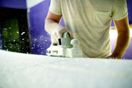 Hand, sanding and surfboard with person in workshop for maintenance, production or repair. Equipment, manufacturing and power tools with small business owner in studio of surf shop for shaping - Powered by Adobe