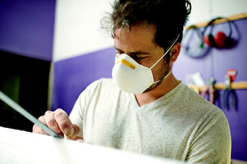 Manufacturing, man and sanding surfboard in workshop for production process, design or creative craftsmanship. Surfer, blank or person with tools for shape, polish or smooth foam with protective mask