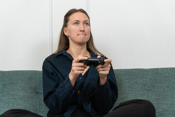 Young woman playing videogames with a focused expression, holding a wireless controller and sitting on a comfortable sofa in her living room, enjoying her leisure time