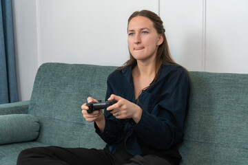 Young woman sitting on a comfortable sofa playing videogames with a wireless controller, concentrating on the game with a serious expression