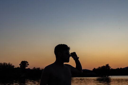 Tourist shielding his eyes from the setting sun while enjoying summer holidays by the lake - Powered by Adobe