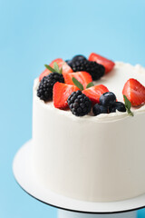 Birthday cake with white cream cheese frosting decorated with fresh raspberries and blackberries. Elegant summer cake with red and black berries on the blue background