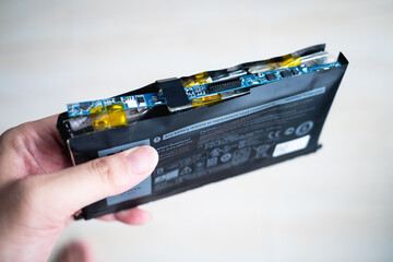 The act of a man extracting a bulging, ruptured battery from his computer serves as a poignant...