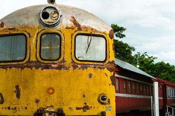 Close-up of an old locomotive and old carriages on a decommissioned railway, the paint cracked, peeled and rusted.
