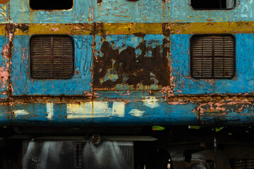 Close-up of an old locomotive and old carriages on a decommissioned railway, the paint cracked, peeled and rusted.