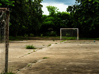 An empty outdoor soccer field with a goal with a net and an old soccer ball on the cement floor. Old sports equipment in a rural park. © Pornpimon