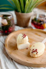 Low-calorie creamy dessert on a stick, artfully drizzled with white chocolate and berry crumbles. Summer healthy snack inspiration.