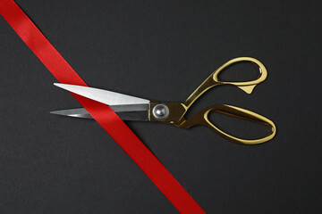 Golden scissors with ribbon on black background, flat design. Place for text.
